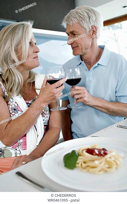 Close-up of a senior couple toasting with wine glasses at the kitchen counter