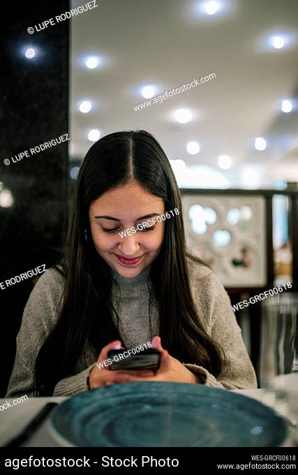 Smiling teenage girl using mobile phone while sitting in restaurant