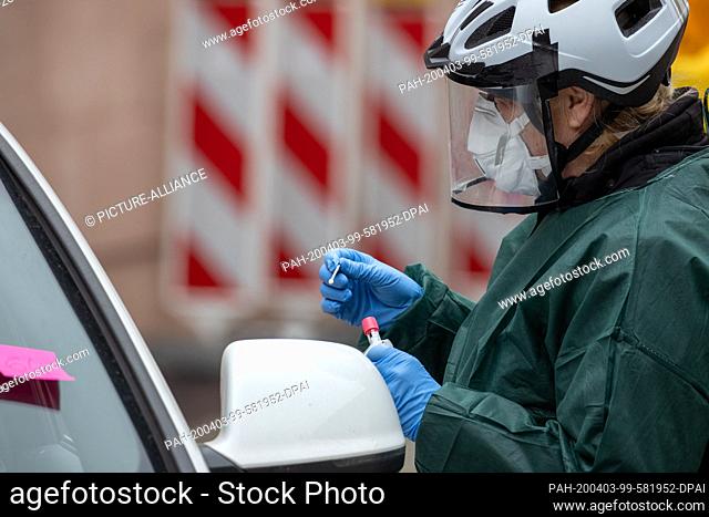 03 April 2020, Bavaria, Nuremberg: An employee of the public health department takes a smear in a corona test centre from a person in his car