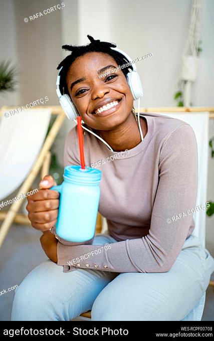 Smiling woman with mason jar sitting on deck chair in living room