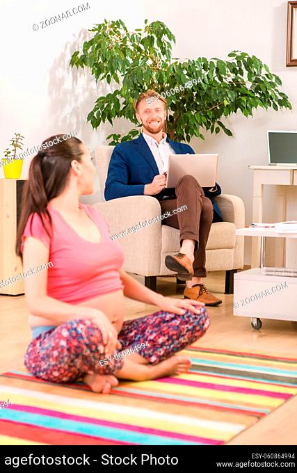 Pregnant woman communicating with her husband while doing yoga at home. Brunette lady and her husband expecting baby soon