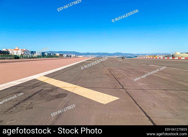 Gibraltar, UK - August 20, 2021. Locals and cars crossing the runway at the Gibraltar Airport with the Rock of Gibraltar in the background