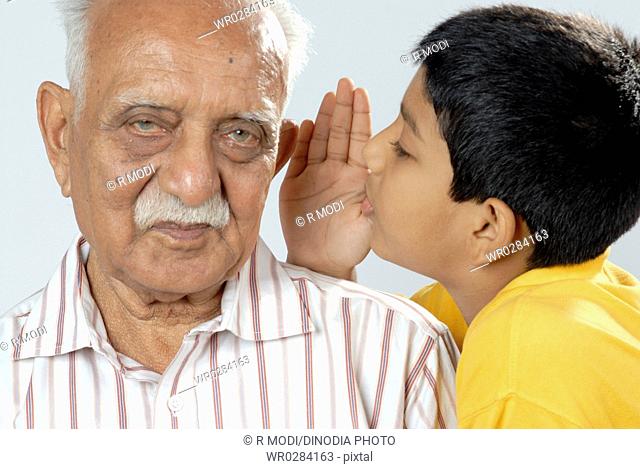 South Asian Indian grandson sharing secret in ear of grandfather MR152