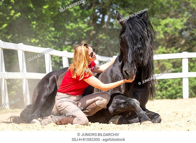 Pure Spanish Horse, Andalusian. Woman smooching with black stallion, lying on a riding place. Germany