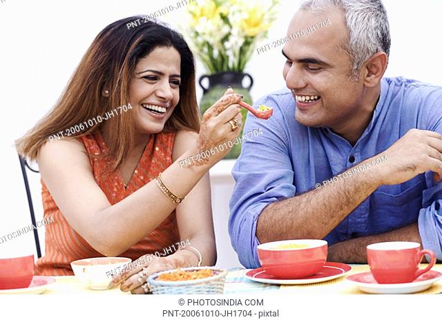 Mid adult woman feeding a spoonful of snacks to a mid adult man