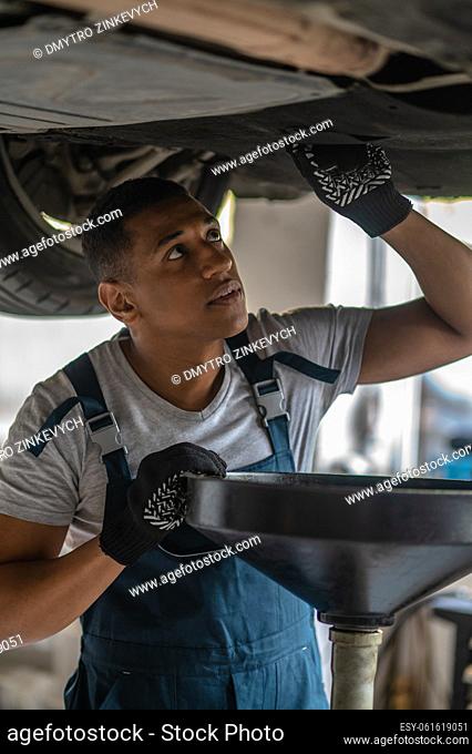 Serious focused automotive service mechanic in work clothes examining the underbody of a client vehicle