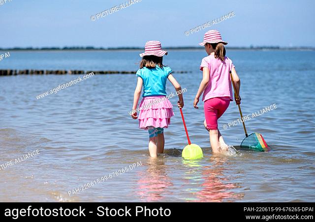 15 June 2022, Lower Saxony, Hooksiel: Two girls play with their landing nets in the shallow waters of the North Sea on the beach in sunny weather