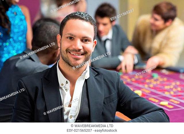 Smiling man sitting leaning on roulette table in casino