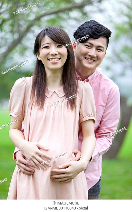 Young man embracing pregnant woman and smiling at the camera