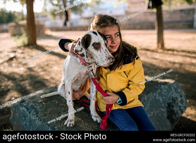Cute girl hugging dog while sitting on rock