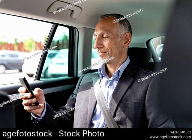 Male professional using smart phone while sitting on back seat in car