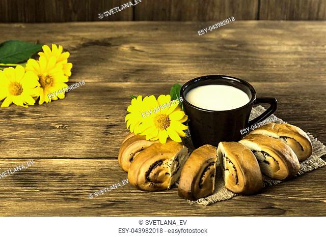 Food. Baking of confectionery. Fresh baked bakery with poppy seeds and a cup of milk for breakfast on the background of the texture of a wooden table