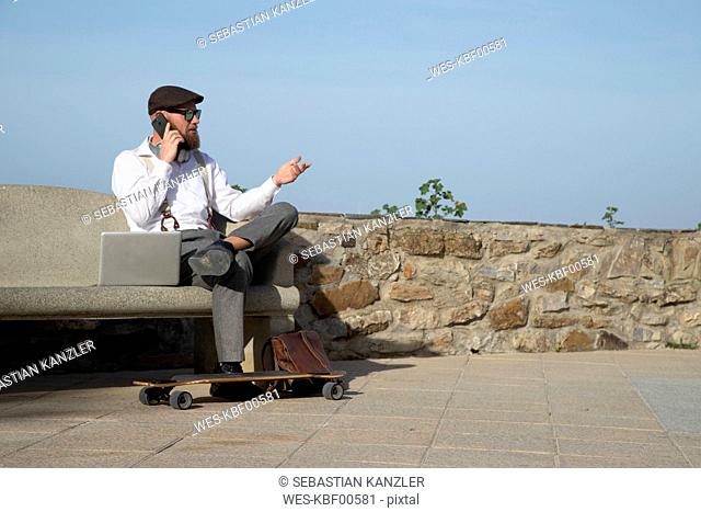 Man on the phone sitting with laptop on a bench