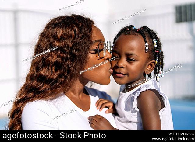 Woman kissing daughter on sunny day