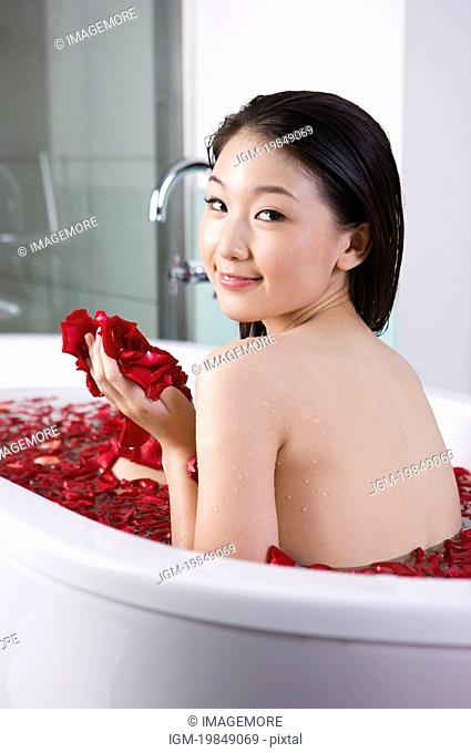 Young woman having the bath with roseleaves and looking at the camera