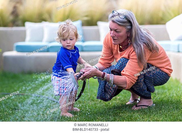 Caucasian grandmother and baby grandson watering lawn with hose