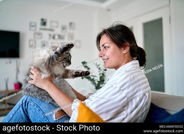 Happy woman stroking cat on sofa at home