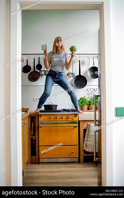 Mature woman standing on stove enjoying in kitchen