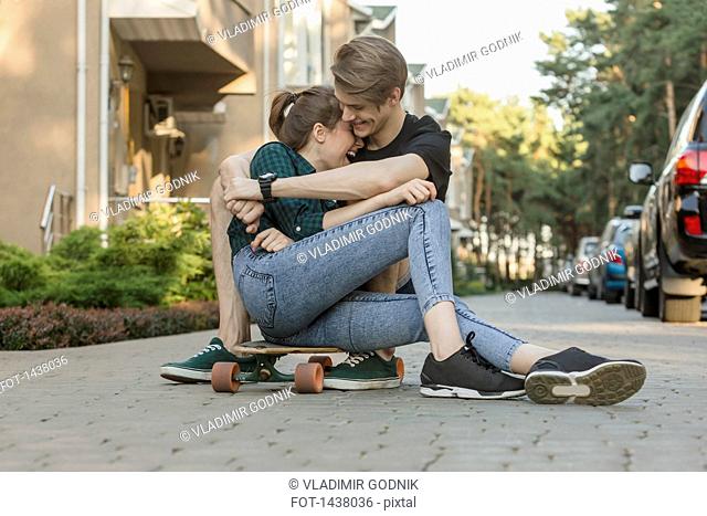 Happy young couple embracing while sitting on skateboard outdoors
