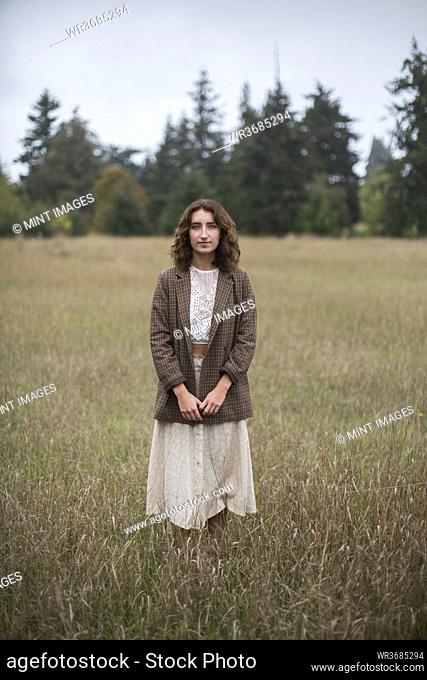 Portrait of seventeen year old girl wearing tweed blazer, standing in field of tall grasses, Discovery Park, Seattle, Washington