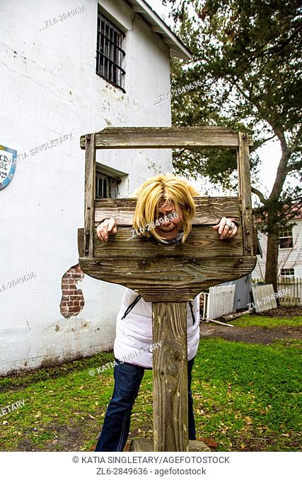 Blond caucasian woman getting in the guillotine and is pretending getting decapitated in an Old village with a guillotine and an old pharmacy apothecary small...