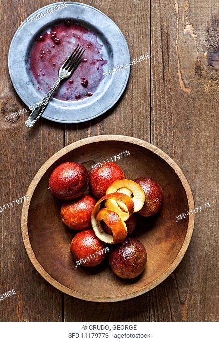 A Wooden Bowl of Blood Oranges with Peel; Dirty Plate with a Fork; From Above