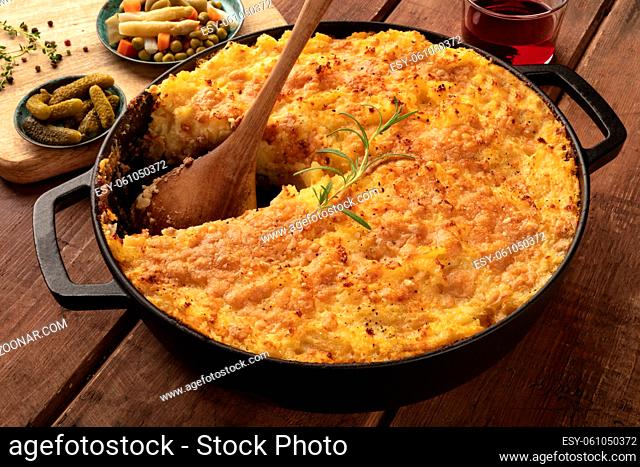 Homemade Shepherd's pie in a cooking pan with pickles and wine on a dark rustic wooden background
