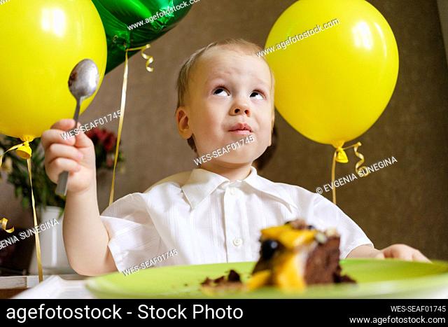 Boy with balloons and cake celebrating birthday at home