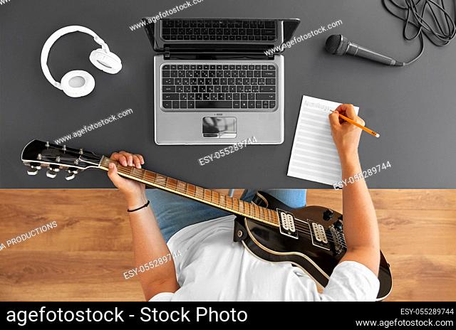 man with guitar writing to music book at table