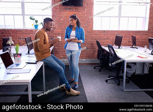 Happy diverse male and female colleagues at work standing discussing over coffee and tablet