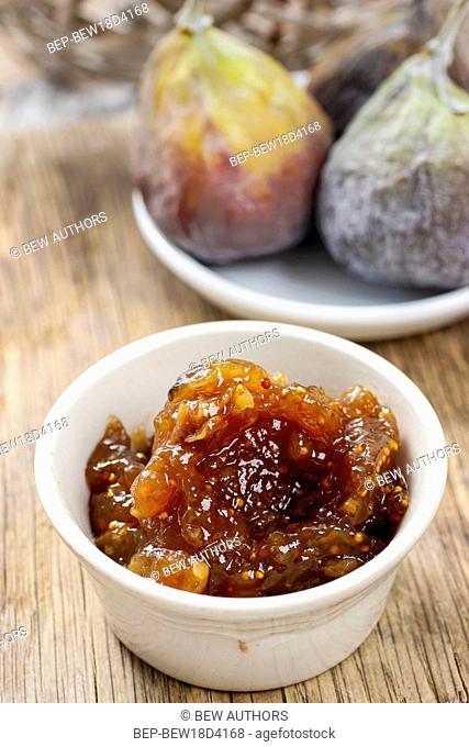 Bowl of fig jam and raw figs on rustic wooden table