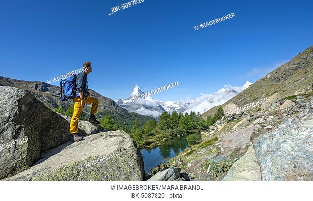 Hiker stands on rocks and looks into the distance, behind Lake Grindij and snow-covered Matterhorn, Valais, Switzerland, Europe