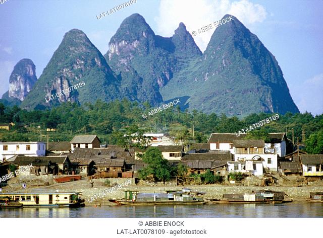 View of houses on hillside. From across river. Water. Pinnacles/ mountain peaks in distance