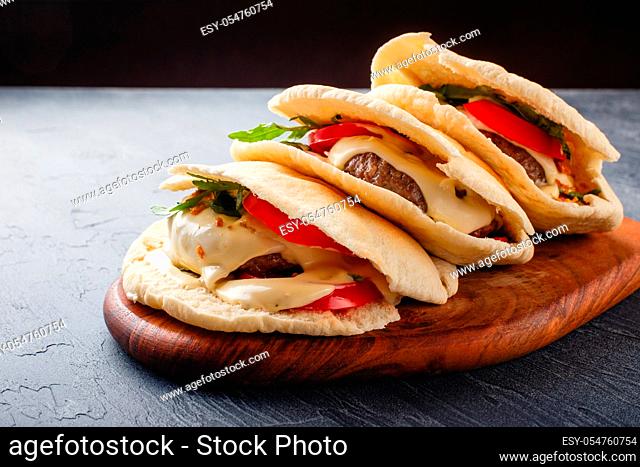 Grilled beef burgers in pita bread with sauce, cheese, tomato and arugula leaves