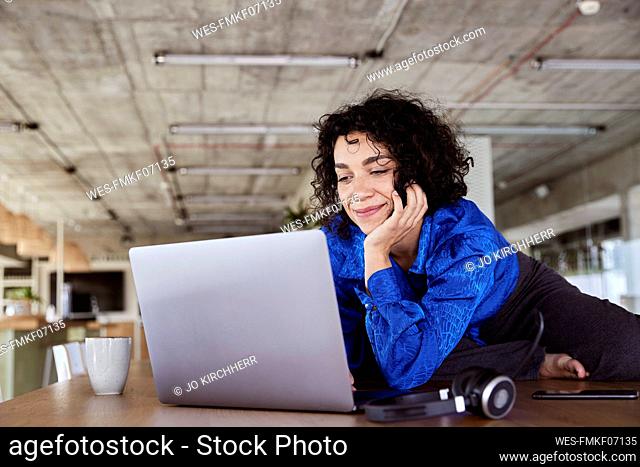 Smiling woman using laptop on table at loft