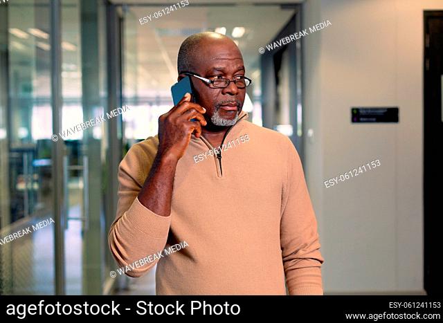 Bald african american mature businessman talking through smartphone walking in corridor at workplace