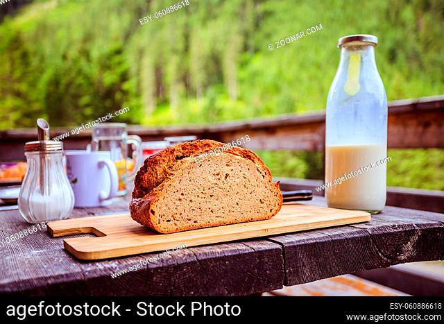 Fresh dark crisp bread for breakfast on an alpine hut. Wooden cutting board and milk in glass bottle