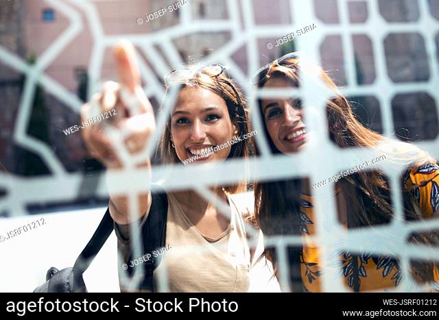 Smiling women pointing toward map while standing at Gothic Quarter in Barcelona, Catalonia, Spain