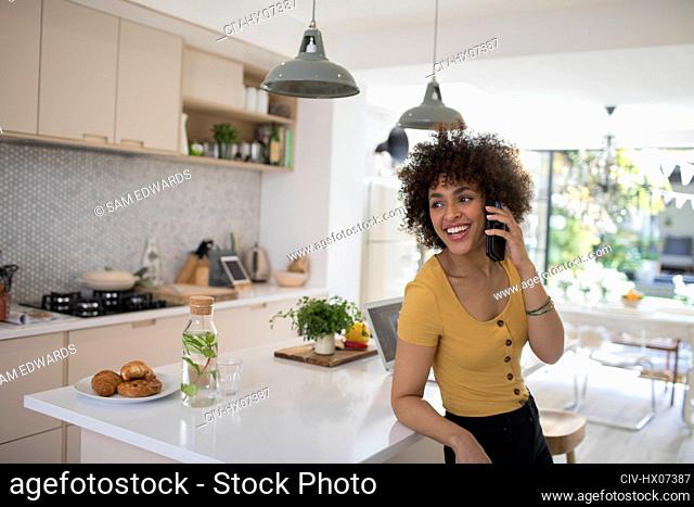 Happy young woman talking on smart phone in kitchen