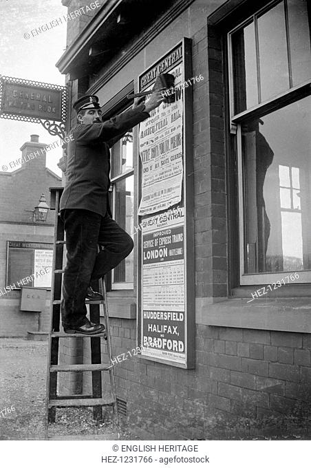 Billposting at Charwelton Station, Northamptonshire, 1904. A Great Central Railway employee sticking up a poster for the County Show outside the waiting room at...