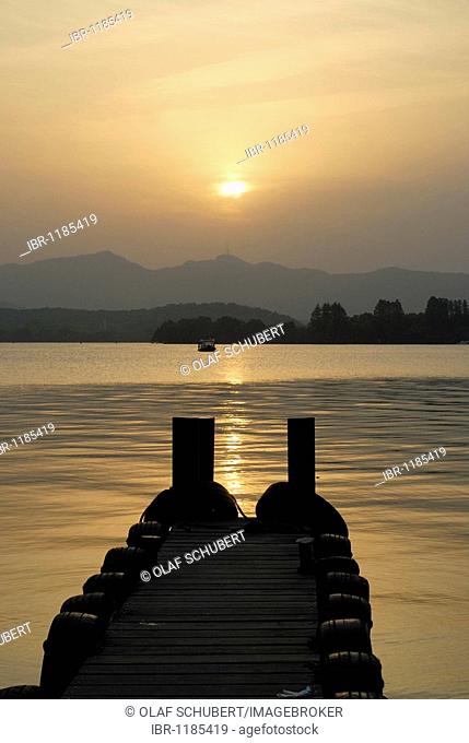 Evening sun with a wooden footbridge at West Lake, Chinese: Xi Hu, in front of a mountain backdrop and boat, Hangzhou, China, Asia