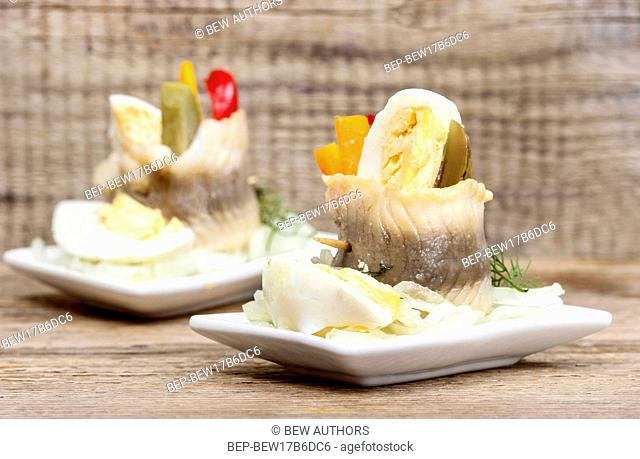 Pickled herring rolls with vegetables on wooden table
