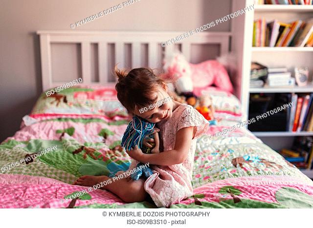 Girl sitting on bed hugging rag doll