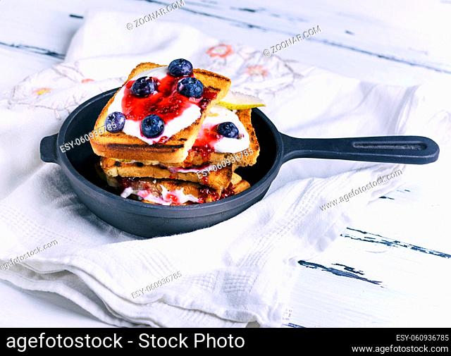 French toast with berries, syrup and sour cream in a black cast-iron frying pan