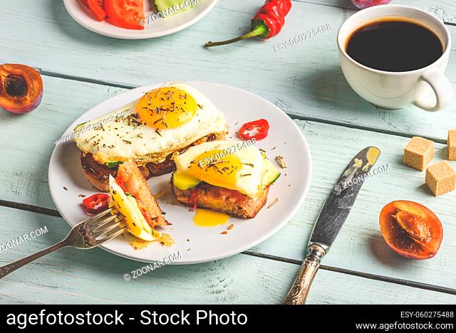 Bruschettas with vegetables and fried egg on white plate, cup of coffee and some fruits over wooden background. Healthy food concept