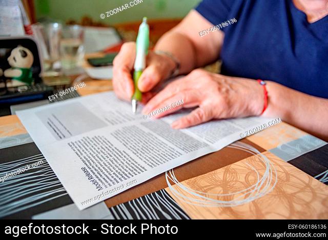 A model release form is being signesd by hands of an eldery female on her dining table