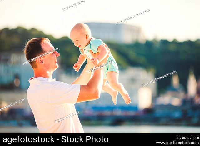 Subject Parenting, summer vacations, father and little son. Young Caucasian dad holds on arms, hugs child overlooking town Kiev and the river on banks of...