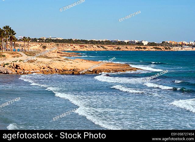 Rocky coast of Flamenco beach in the Orihuela Costa. Surf Mediterranean Sea, winter tropical climate sunny day. Province of Alicante, Costa Blanca, Spain