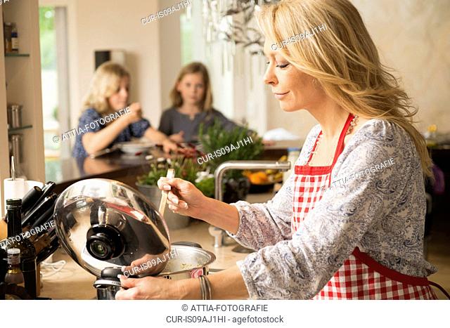 Mother preparing food with daughters in background