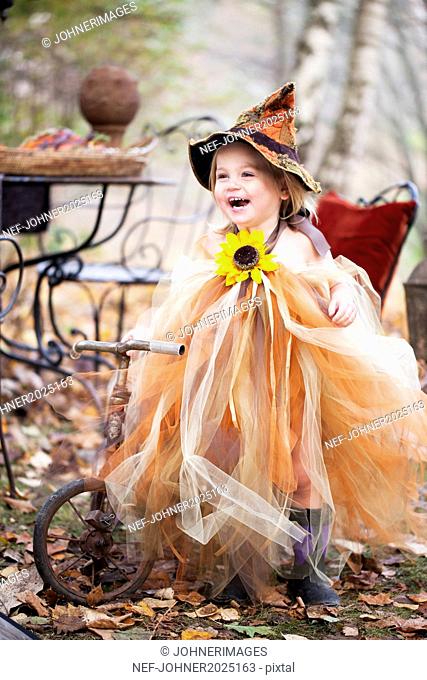 Laughing girl wearing witch hat on tricycle
